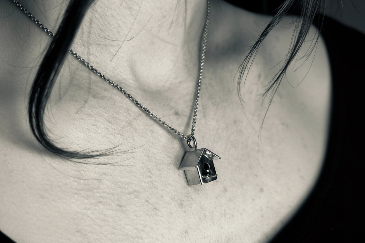 Silver birdhouse pendant necklace on a person's neck