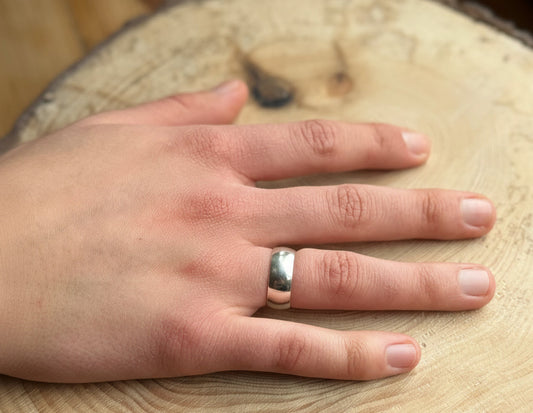 Wide silver ring band, a-shaped profile on hand resting on wood