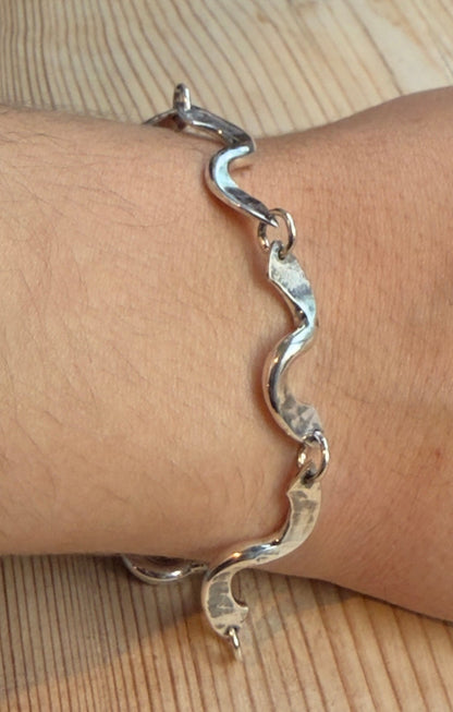 Forged twist link bracelet worn on a wrist beside a white lace sleeve, showing its polished, wave-like links.