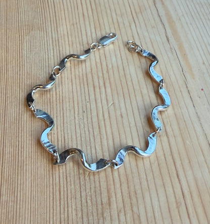 Forged twist link bracelet laid open on wood, showing its wave-like links and lobster clasp fastening.
