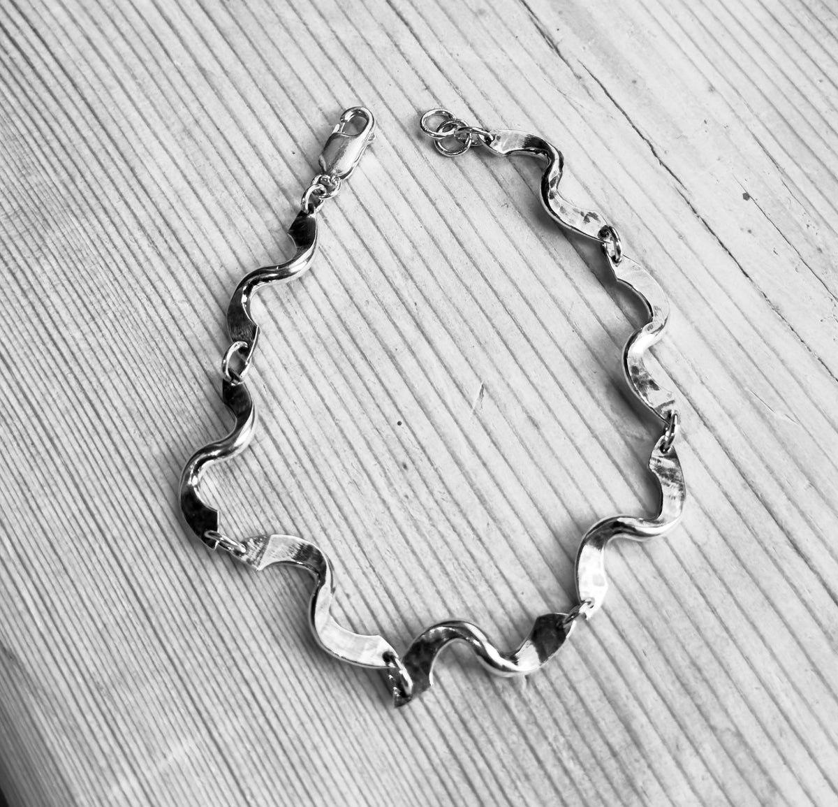  Black-and-white view of the forged twist link bracelet laid open on wood, highlighting its hammered texture.
