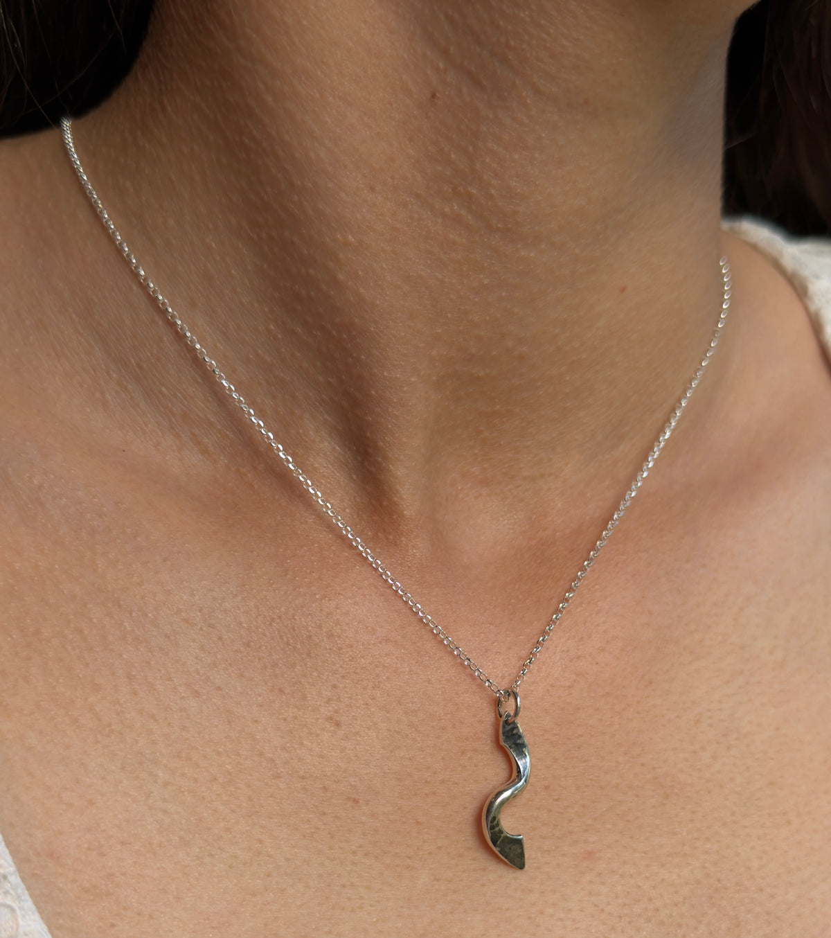 Close-up of a polished silver twist pendant worn on a fine chain, showing its curved shape and hammered texture.