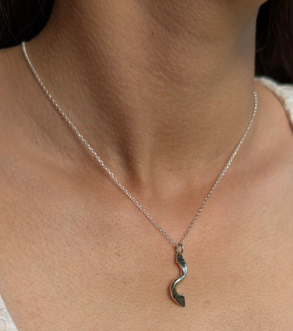 Close-up of a polished silver twist pendant worn on a fine chain, showing its curved shape and hammered texture.