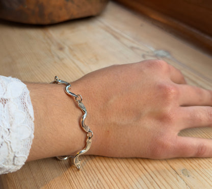 Angled view of a forged twist link bracelet worn on a wrist, with a hand resting on a wooden surface.