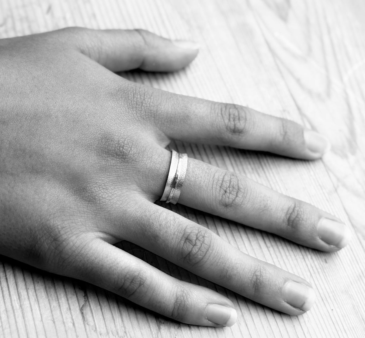 Black-and-white view of the frosted spinner ring worn on a hand resting on a wooden surface.