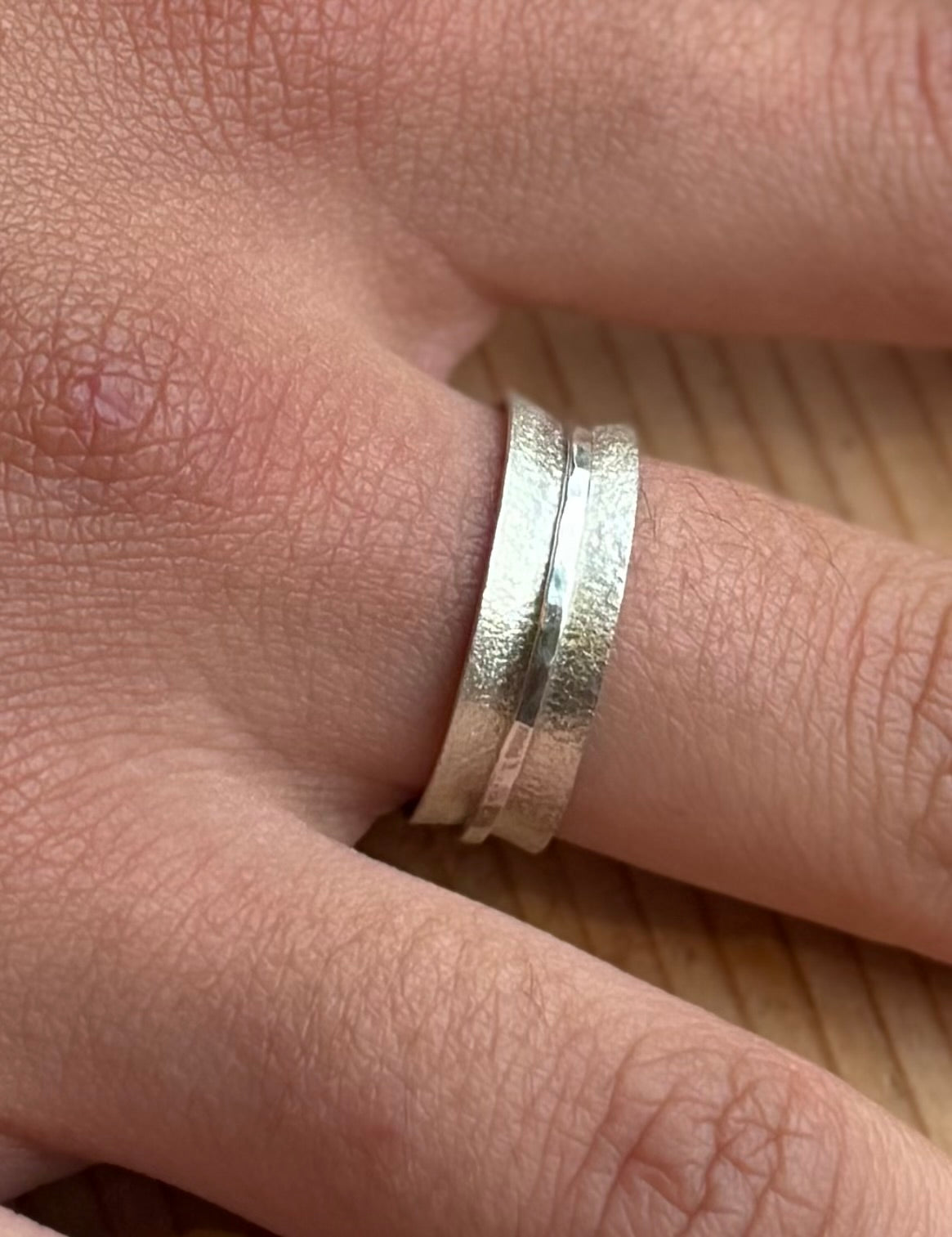Angled close-up of the frosted spinner ring worn on a finger, highlighting the textured main band and narrow spinning band.