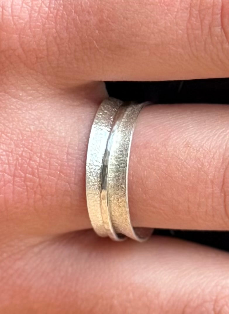 Close-up of a frosted domed spinner ring worn on a finger, showing the fine hammered band around its centre.