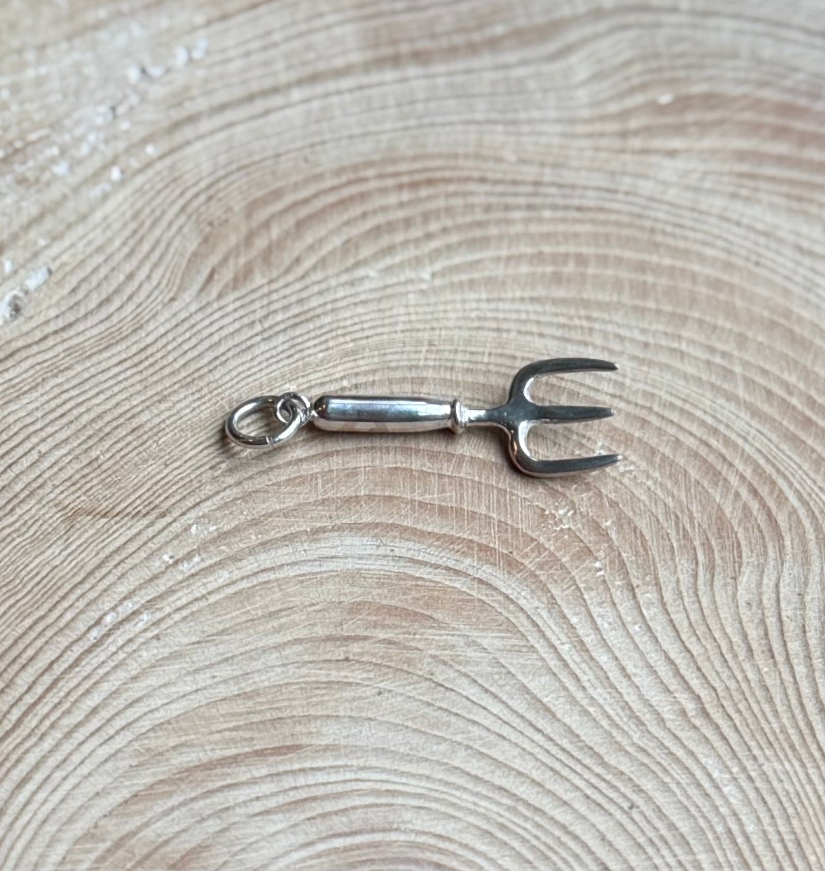 Silver hand fork charm on wood
