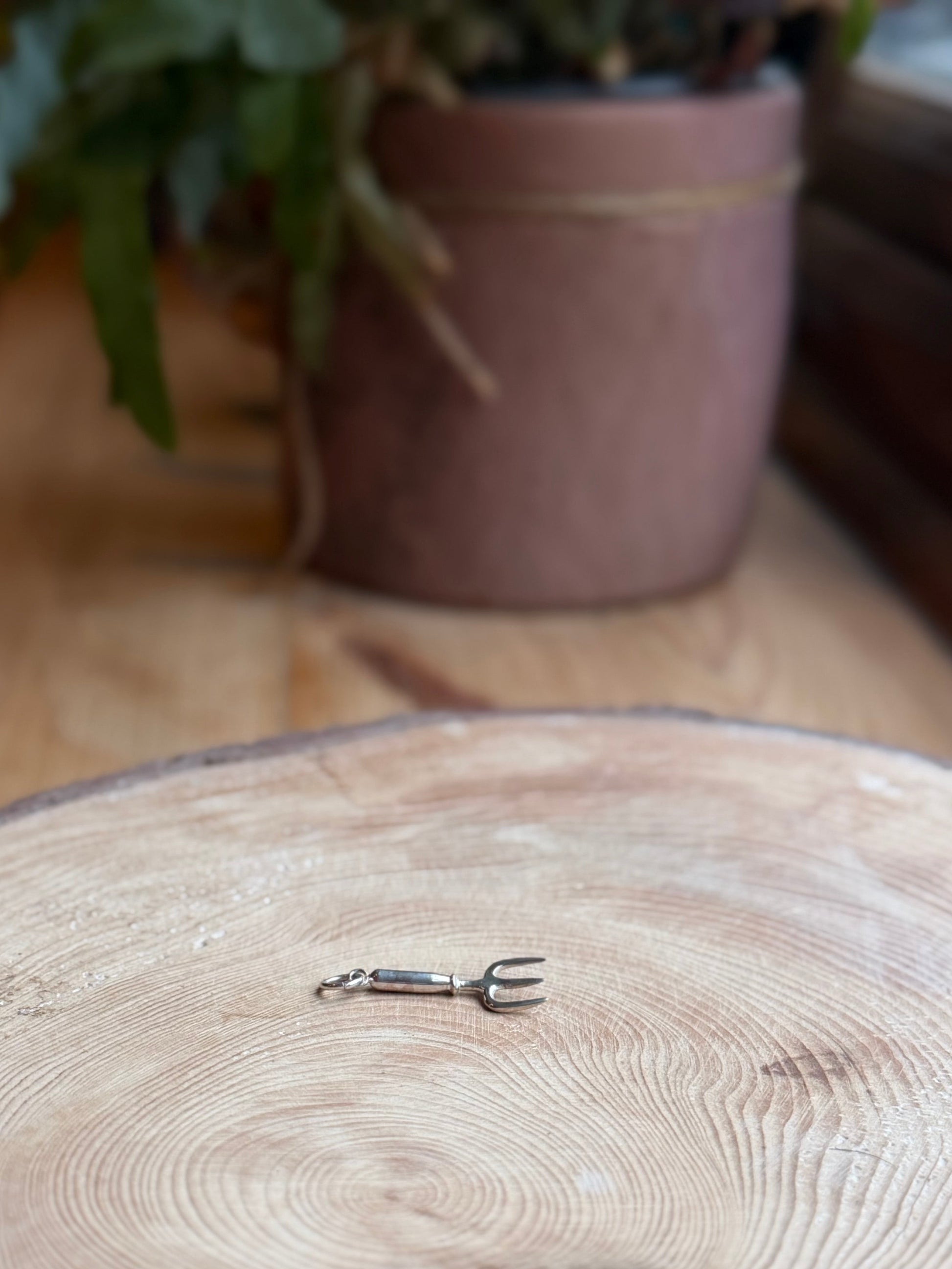 Silver hand fork charm sat on wood with a plant pot behind