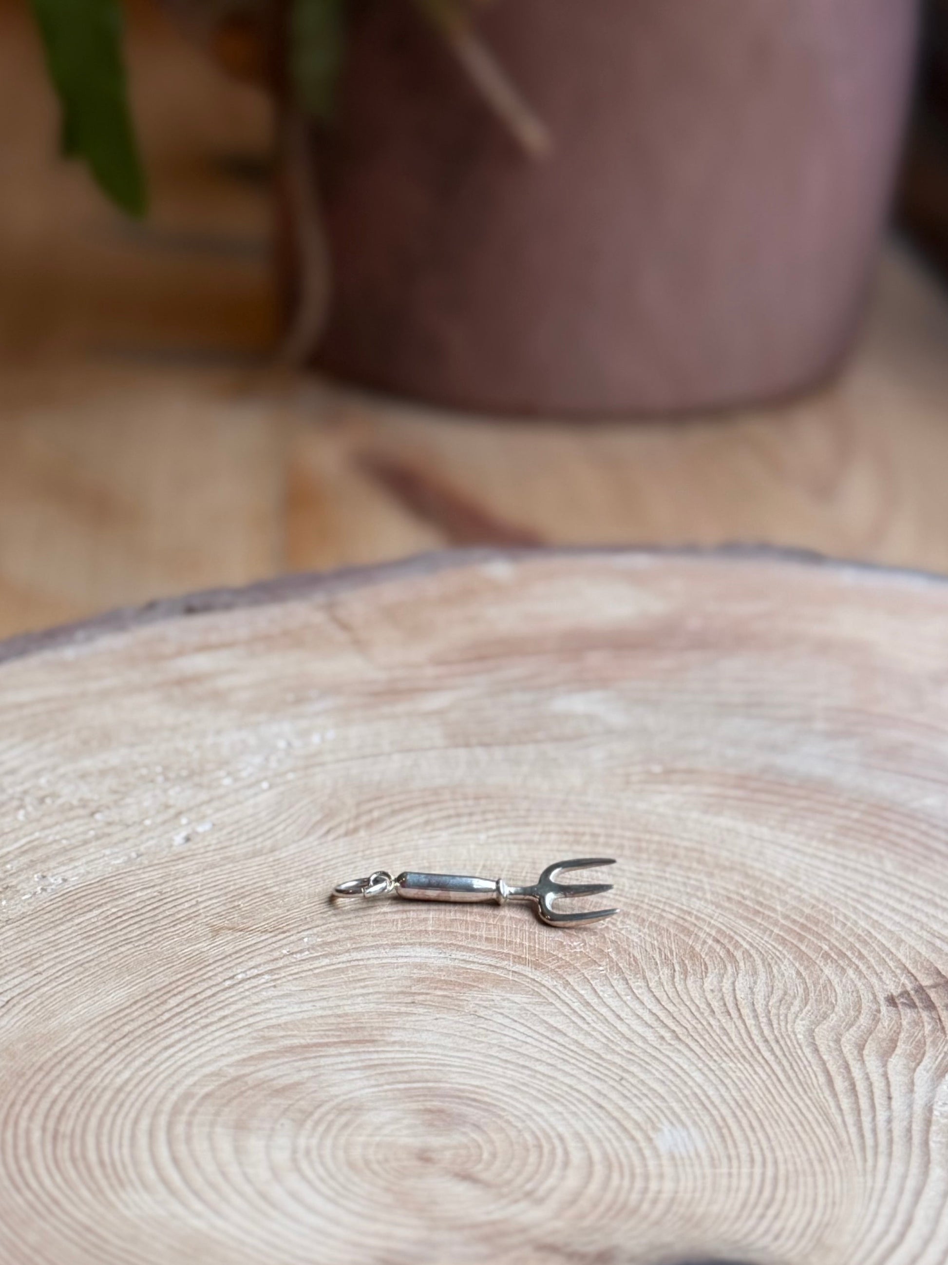Silver hand fork Garden charm on wooden block with plant pot in the background