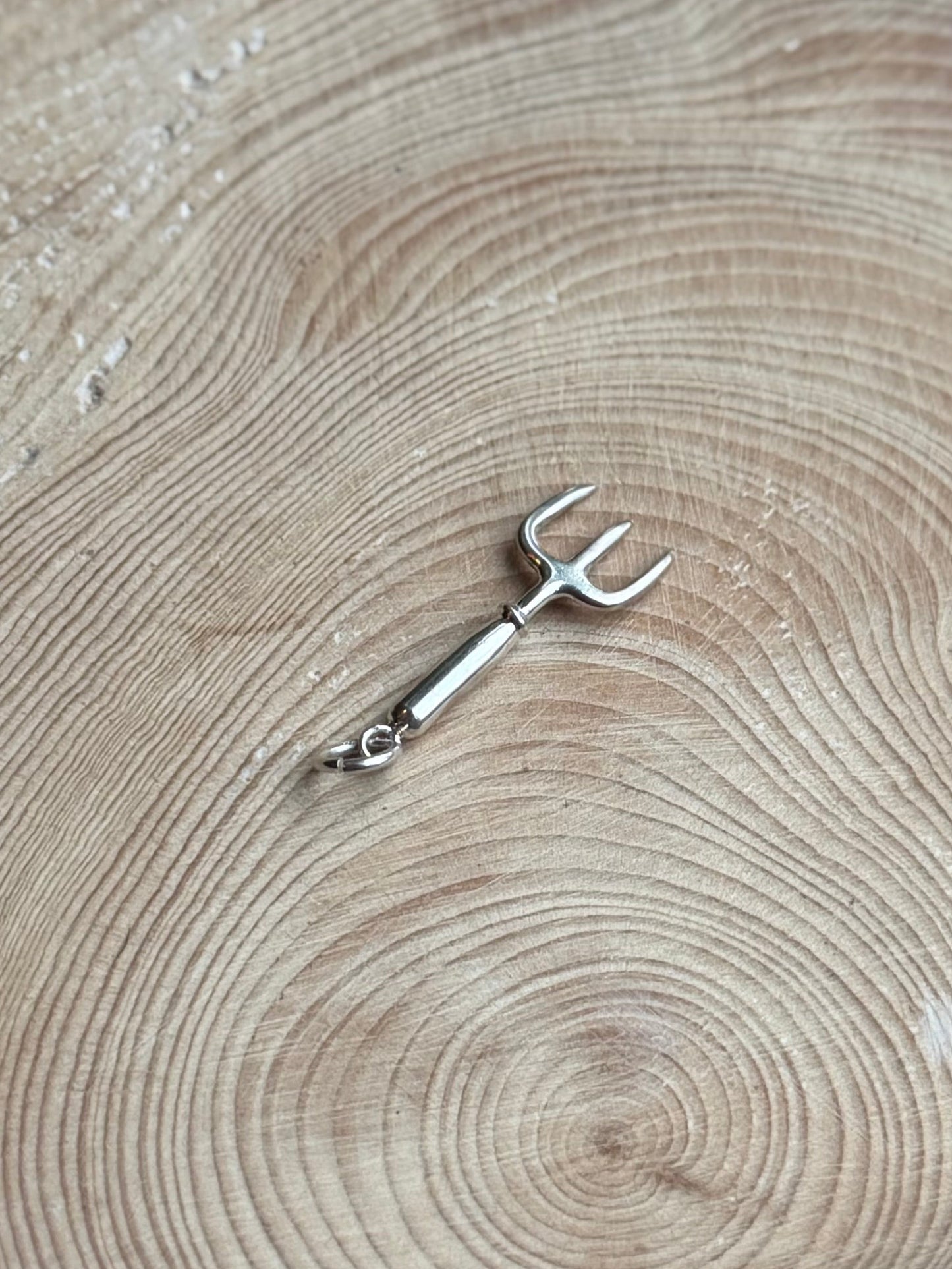 Silver hand fork charm on wooden background