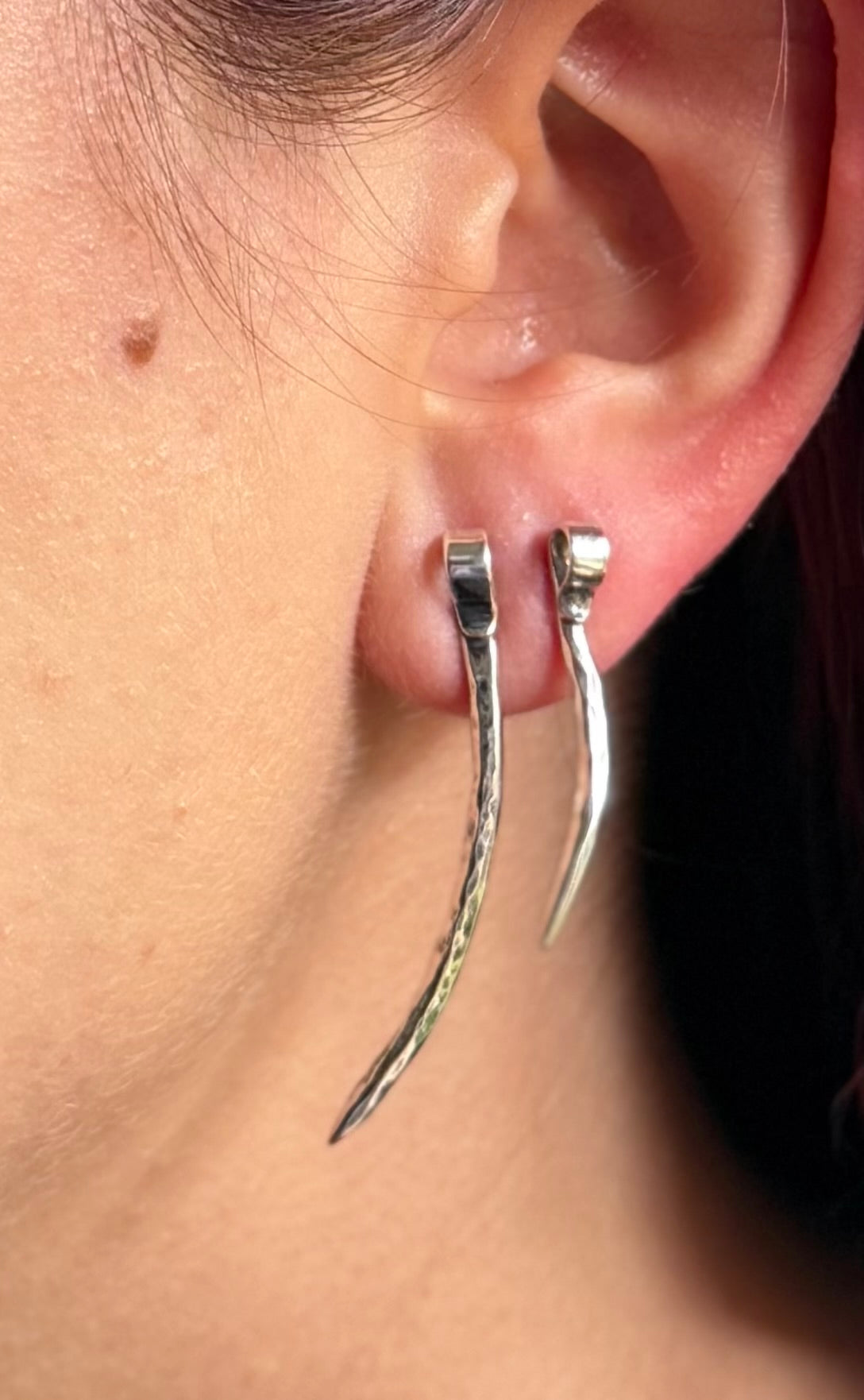 Long and medium forged silver spike studs worn together on an earlobe, showing their contrasting lengths.