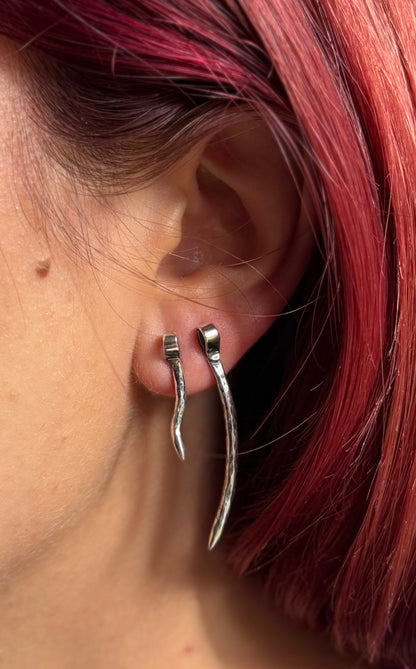 Long and smaller silver spike studs worn together beside red hair, illustrating mixed-size ear styling.