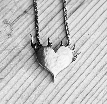 Black and white close-up of the silver Love Set on Fire pendant on wood, showing its satin heart and oxidised flames.