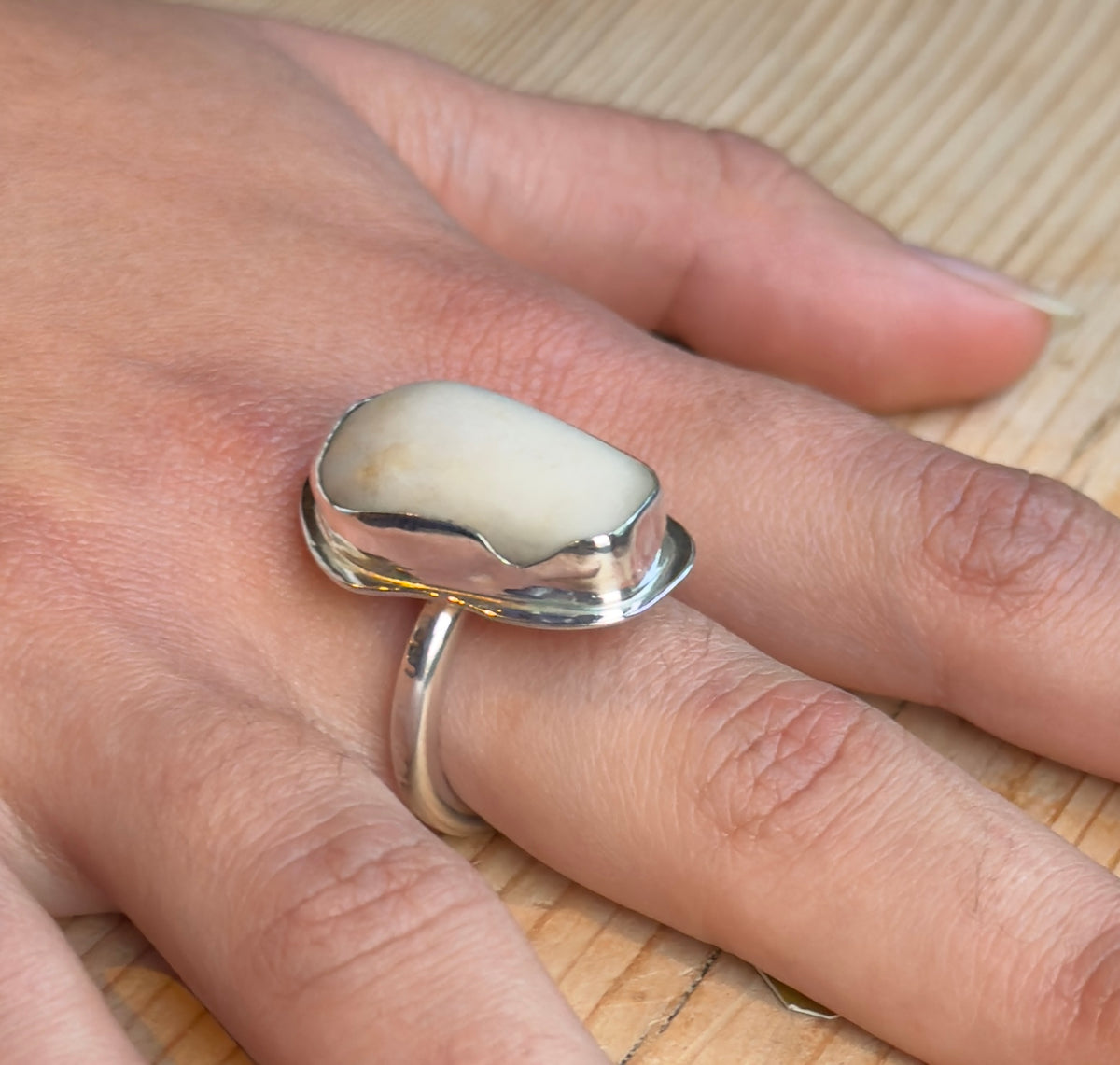 Close-up side view of a pale beach pebble ring, showing its raised sterling silver setting and softly hammered round-profile band.