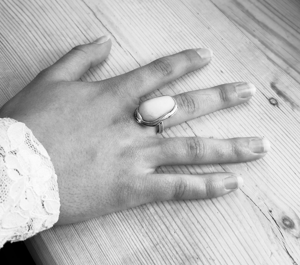 Black-and-white view of a beach pebble and sterling silver ring worn on a hand, showing the smooth stone and irregular silver setting.