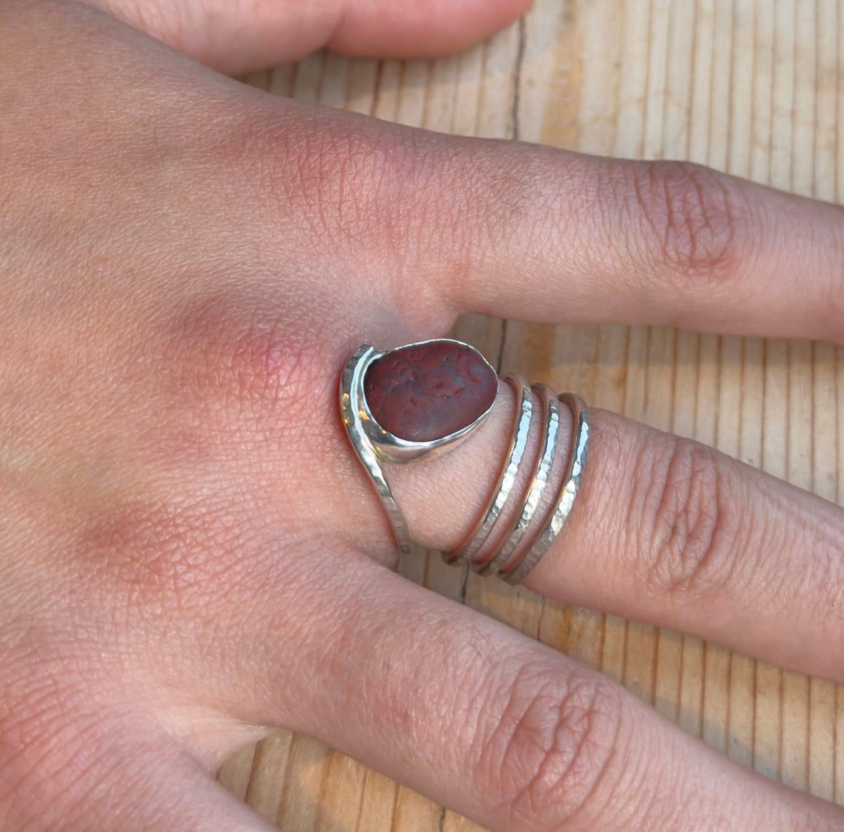 Reddish-brown beach pebble spiral ring worn on a finger, showing the silver setting and hammered band wrapping around the finger.
