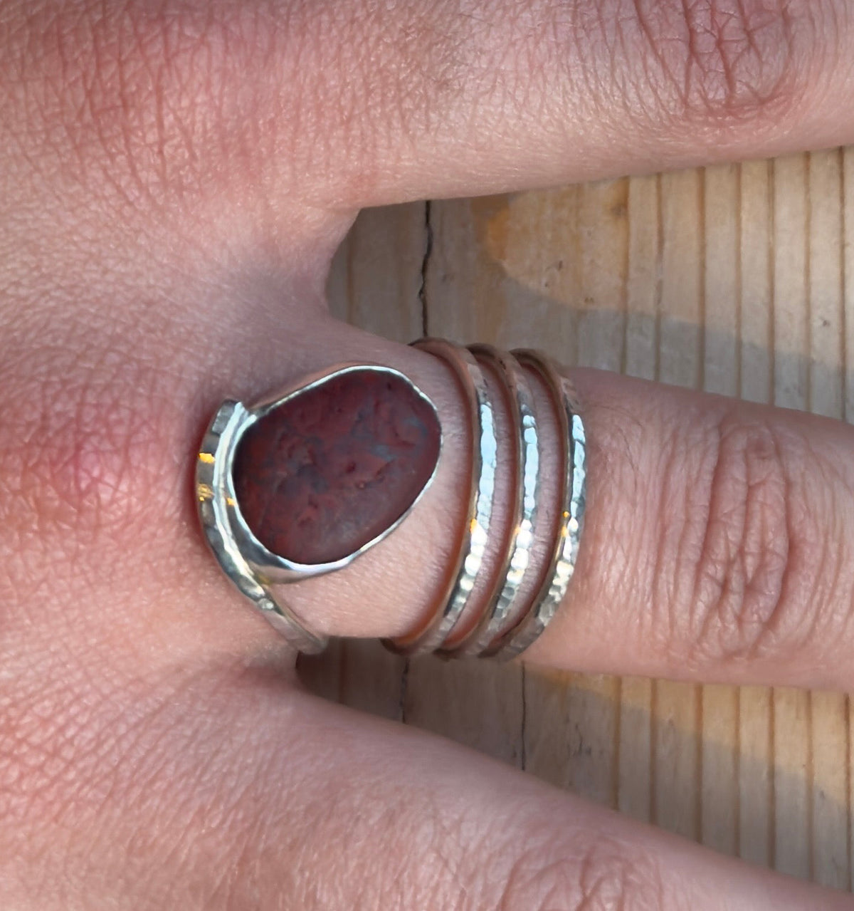 Top-down close-up of a pebble spiral ring, showing the reddish-brown stone beside three hammered silver coils.
