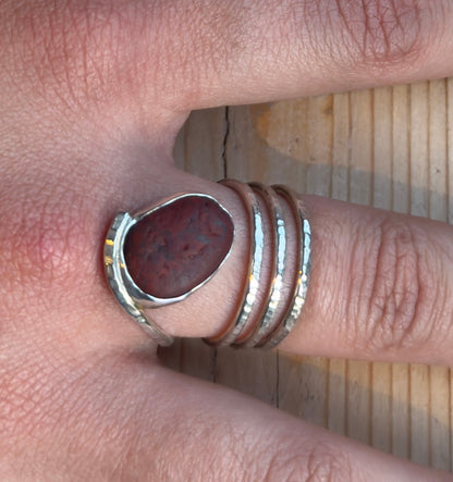 Top-down close-up of a pebble spiral ring, showing the reddish-brown stone beside three hammered silver coils.