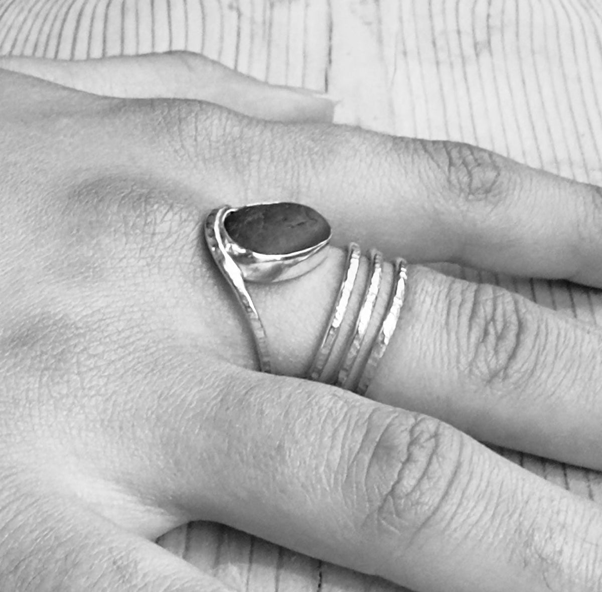 Black-and-white close-up of a beach pebble spiral ring worn on a finger, highlighting the silver setting and hammered coils.