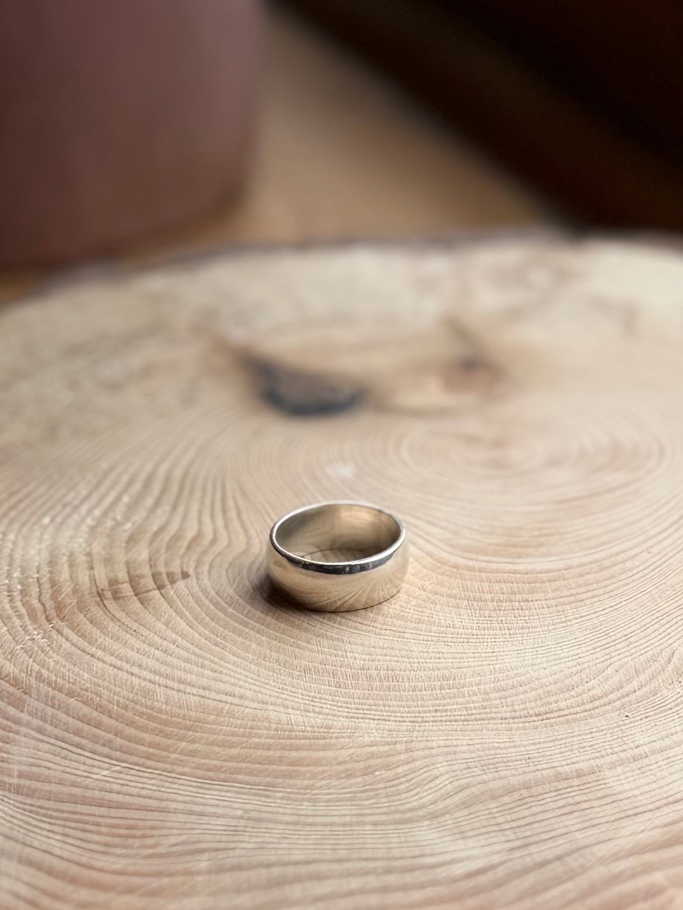 Wide silver ring band, a-shaped profile on wood