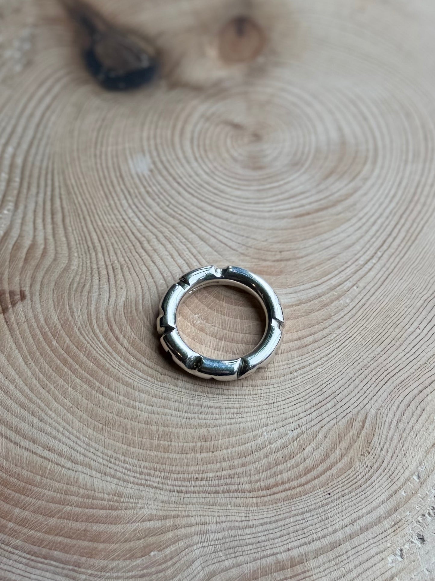 Silver round profile ing on hand, resting on wood
