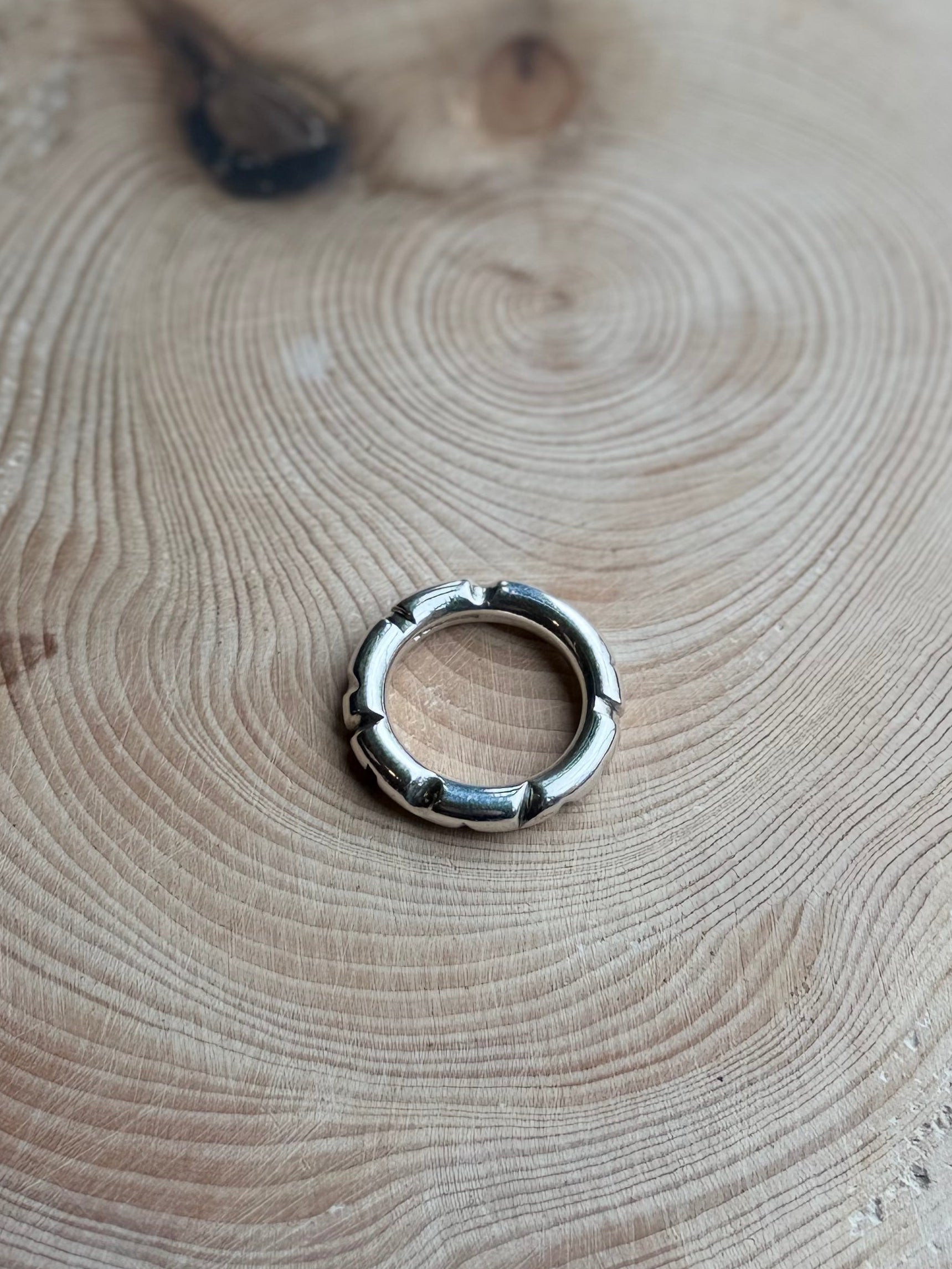 Silver round profile ing on hand, resting on wood
