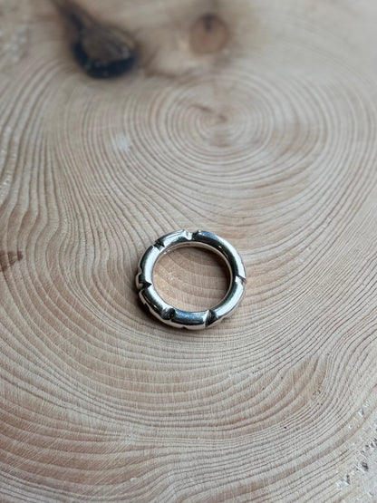 Silver round profile ing on hand, resting on wood

