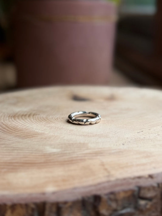 Silver round profile ring with filed shapes, on hand, resting on wood