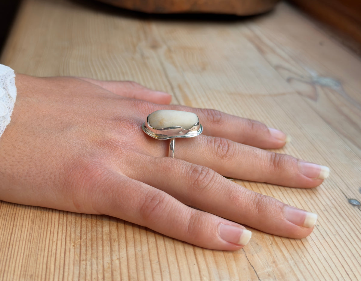Side view of a beach pebble and sterling silver ring worn on a hand, showing the height of the stone above the slender band.