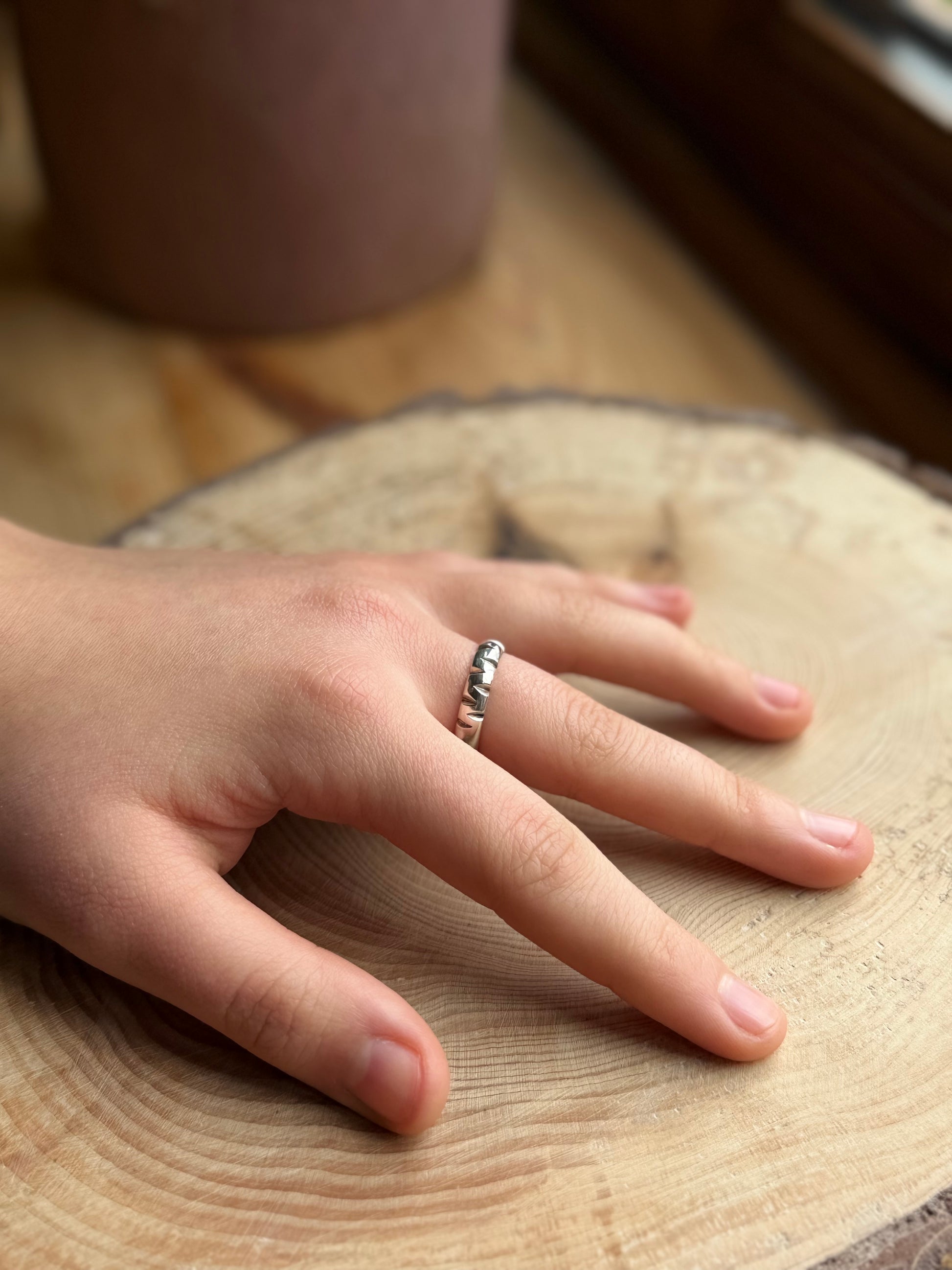 Silver ring with triangular cut outs on hand resting on wood