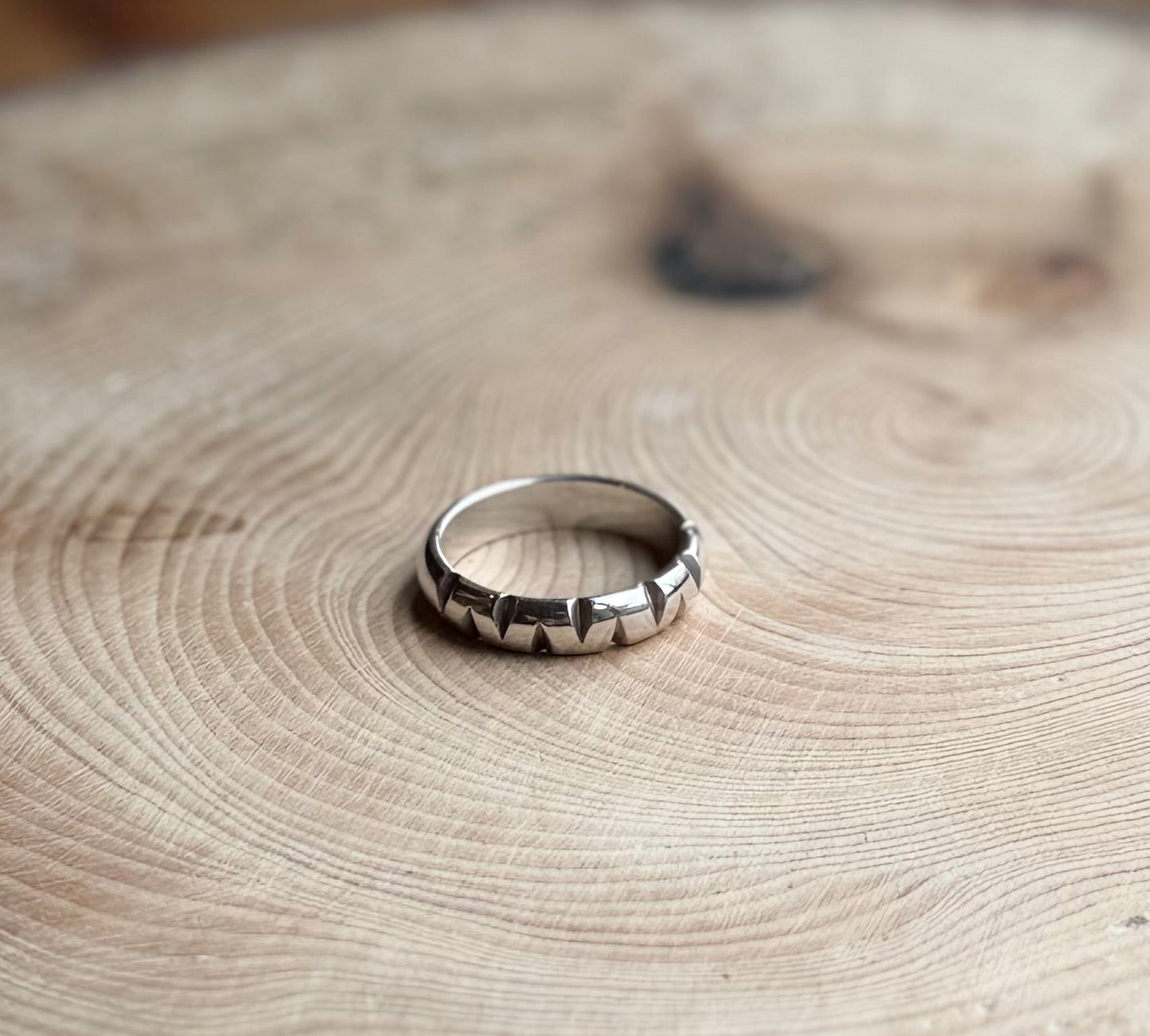 Silver D-shaped ring band with triangular cutouts, on wood