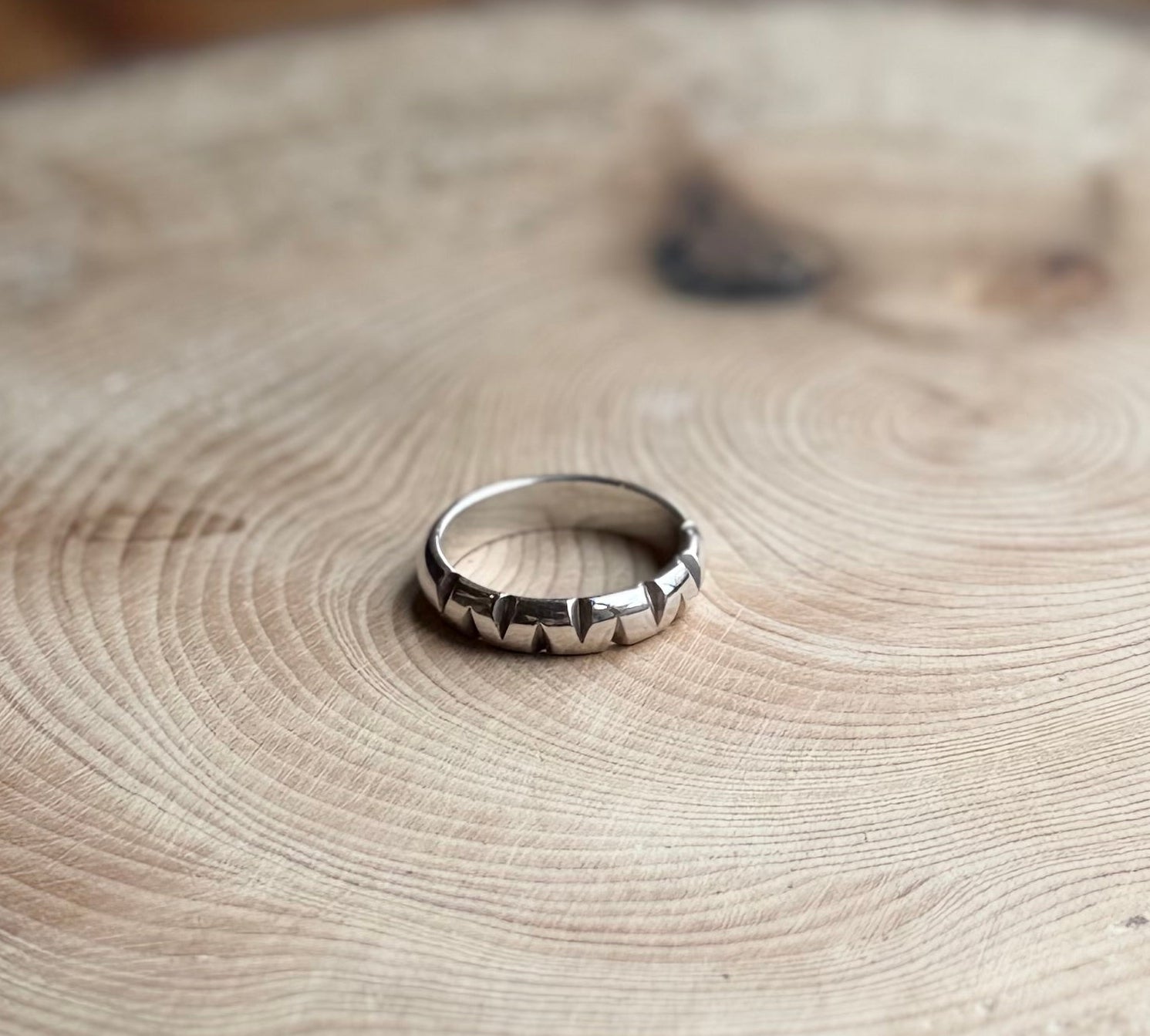 Silver D-shaped ring band with triangular cutouts, on wood