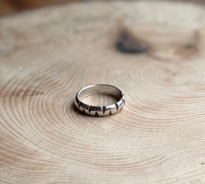 Silver D-shaped ring band with triangular cutouts, on wood