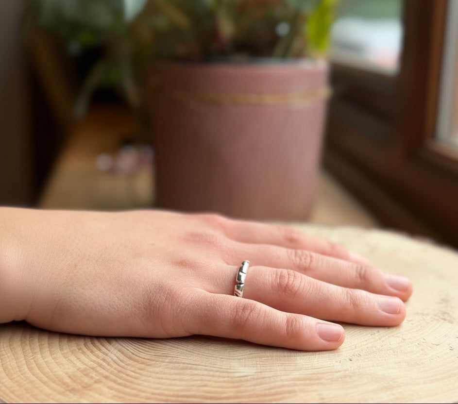 Silver round profile ring with filed shapes on hand, resting on wood
