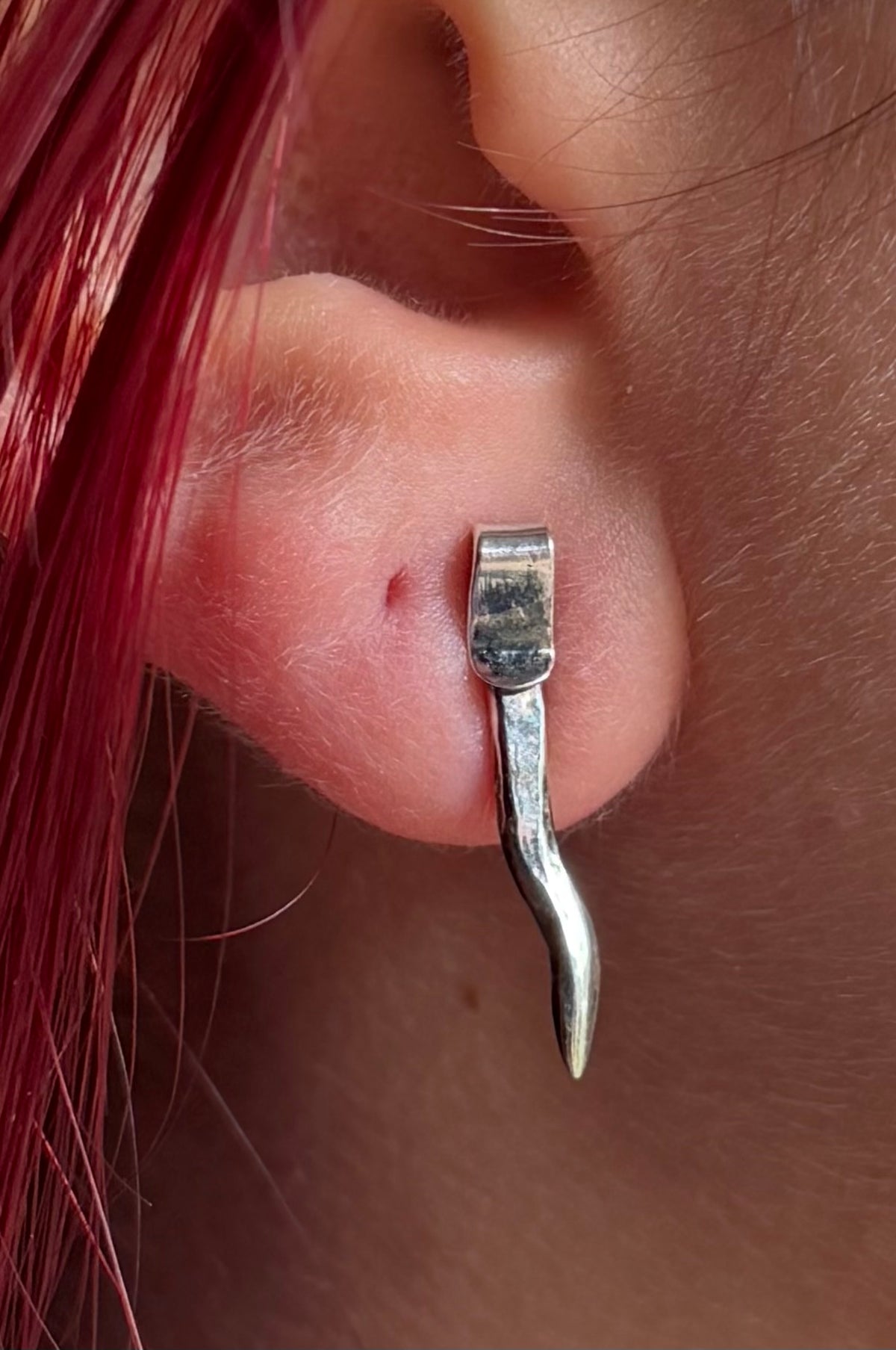 Small spike stud in model’s ear, with bright red hair.