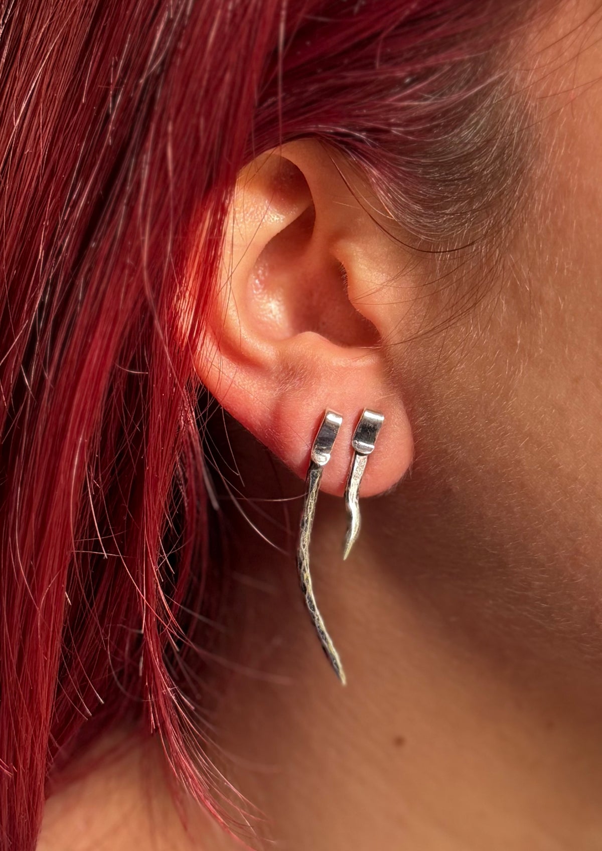Two spike studs in model’s ear, she has bright red hair.