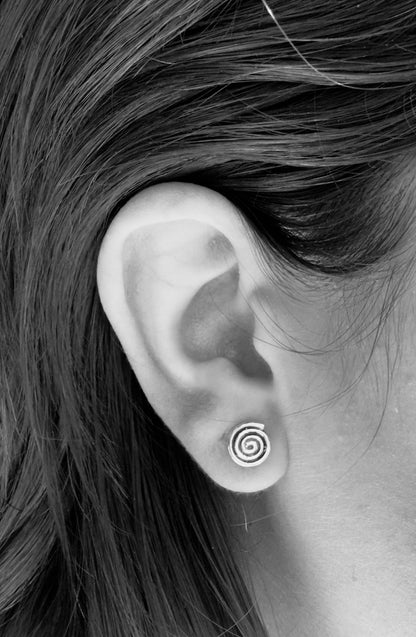 Black-and-white close-up of a silver spiral stud earring worn on an earlobe, showing bright silver curves and dark oxidised detail.