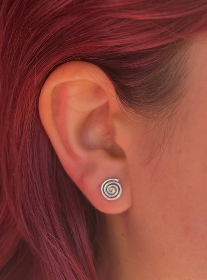 Colour close-up of an oxidised silver spiral stud earring worn beside red hair, showing its coiled design.