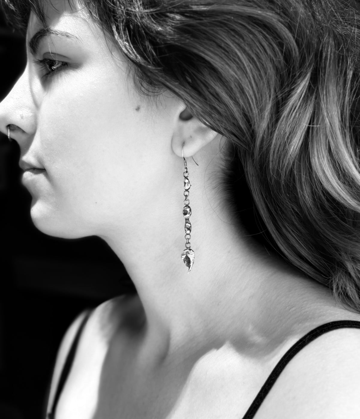 Black-and-white side portrait showing an Alchemy triple silver nugget drop earring worn beside the neck.