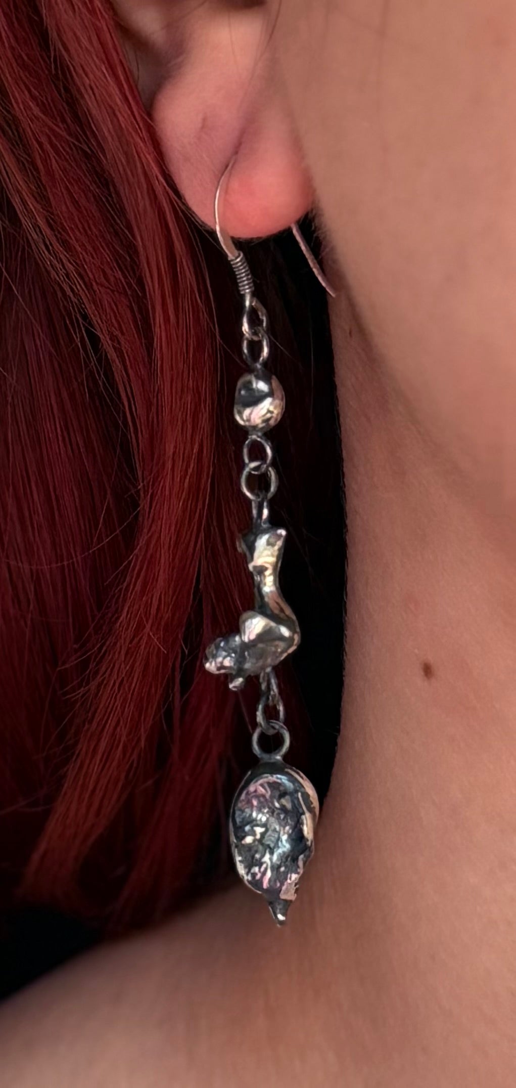 Colour detail of an Alchemy triple nugget earring worn beside red hair, highlighting the irregular silver textures and connecting rings.
