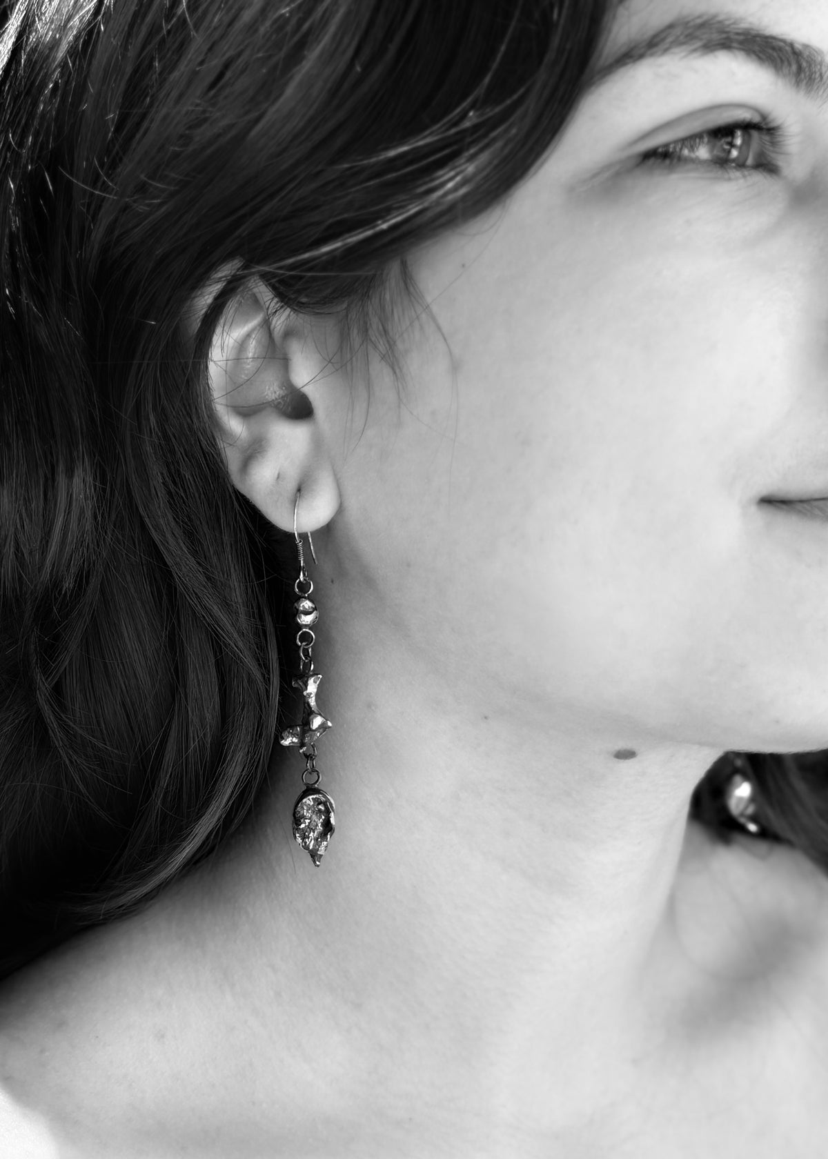Black-and-white portrait showing the other Alchemy drop earring, with three individually shaped silver nuggets.