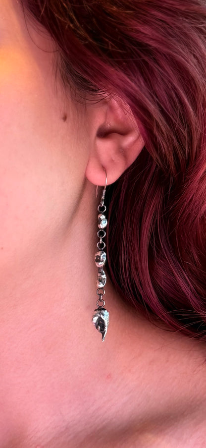 Colour close-up of a triple silver nugget drop earring worn beside red hair, showing its sculptural shapes and reflective surfaces.