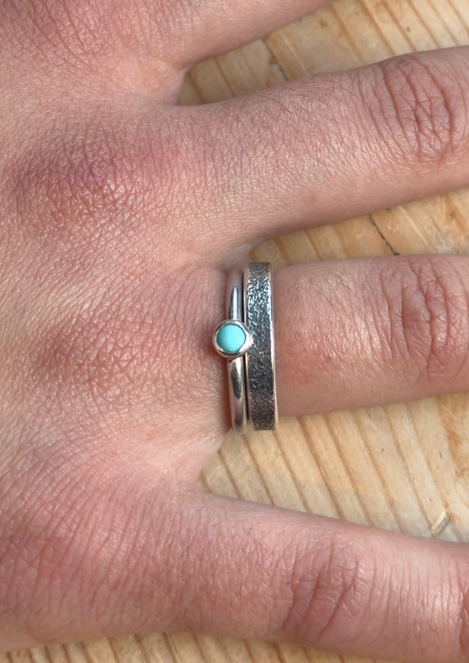 Turquoise cabochon silver ring stacked beside a wider textured silver band on a finger.