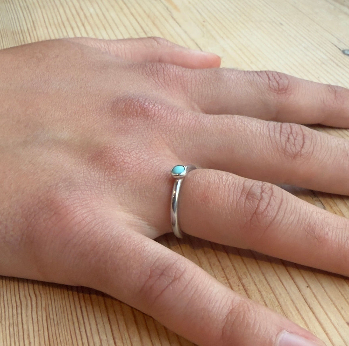 Angled view of a turquoise cabochon ring worn on a hand, showing its polished silver round-profile band.