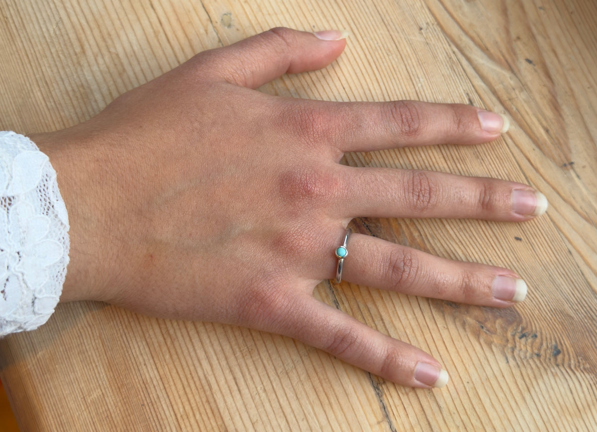 Full hand resting on wood, wearing a delicate silver ring with a small turquoise cabochon.