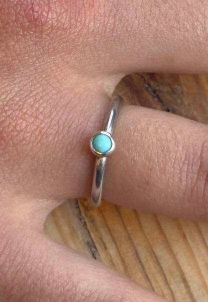 Close-up of the round turquoise cabochon in its silver setting and polished band, worn on a finger.
