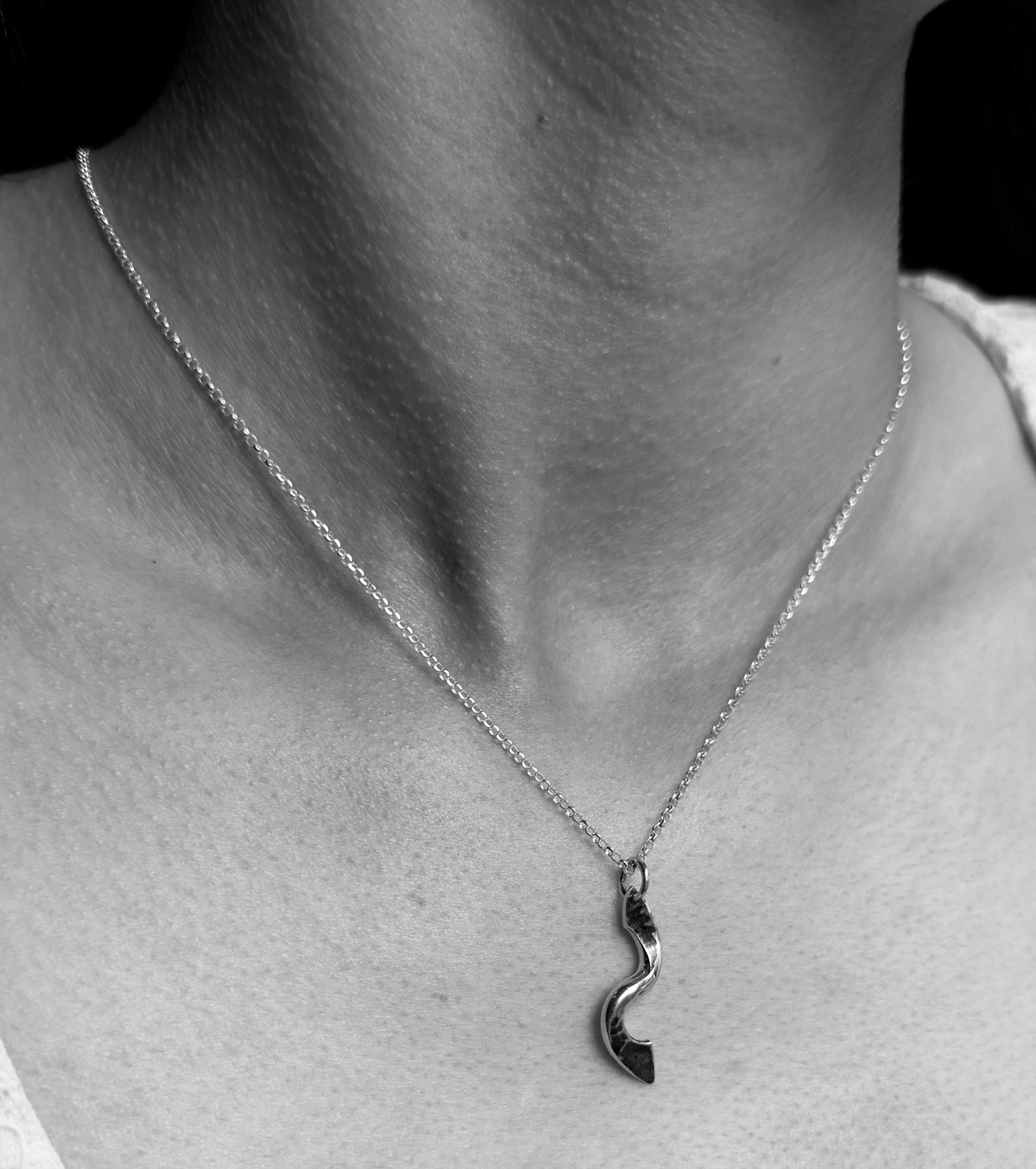 Black-and-white close-up of a forged silver twist pendant and fine chain worn at the neckline.