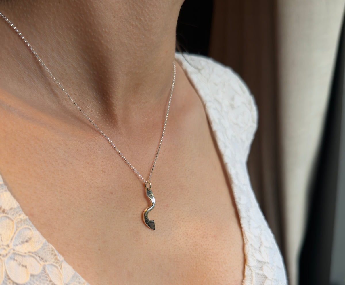 Forged silver twist pendant on a fine chain, worn with a white lace top and viewed from an angle.