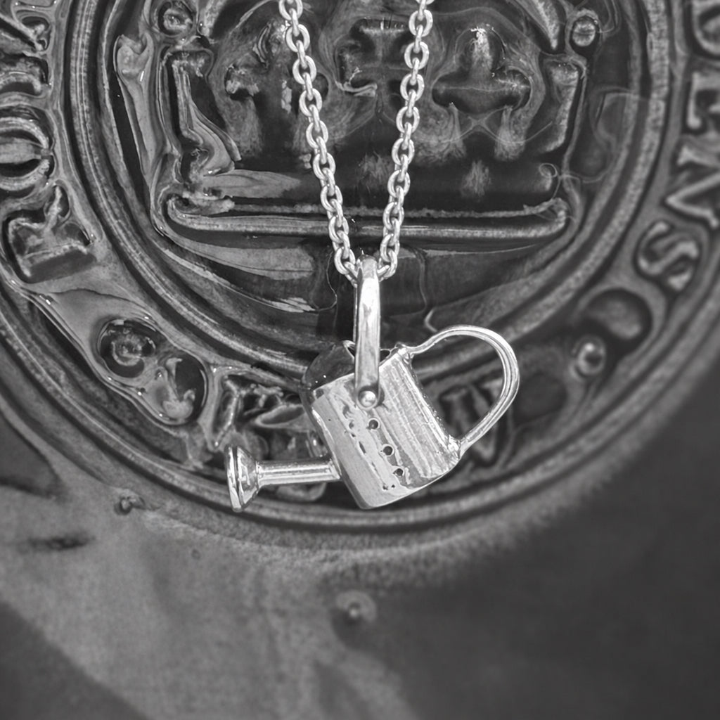 Watering can pendant made of silver draped over a plant pot